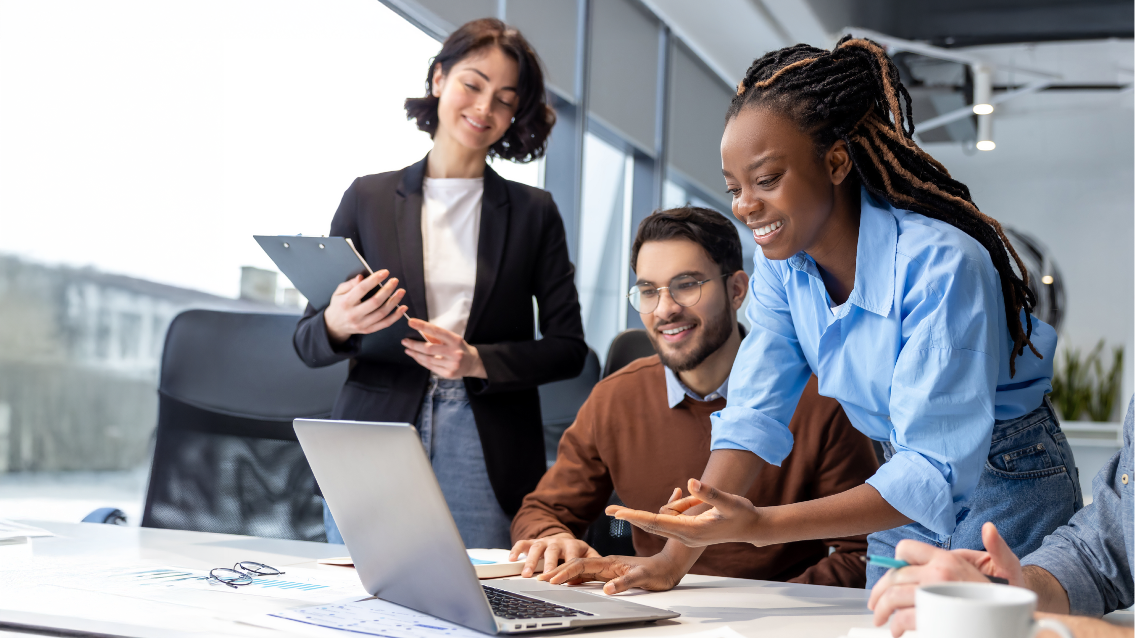 Diverse young professionals collaborating around a laptop in a modern office, reviewing data charts on a conference table