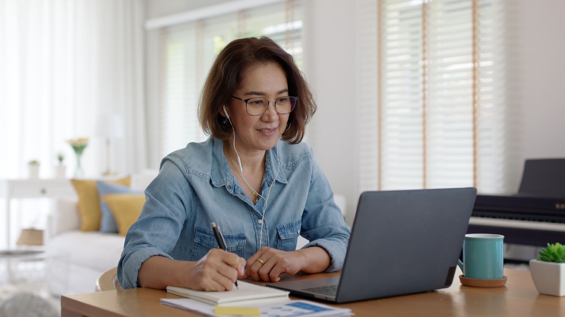 Adult learner taking online class at home, writing notes with laptop and earbuds